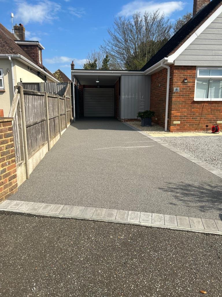 Grey driveway leading to a garage with a contrasting light block border